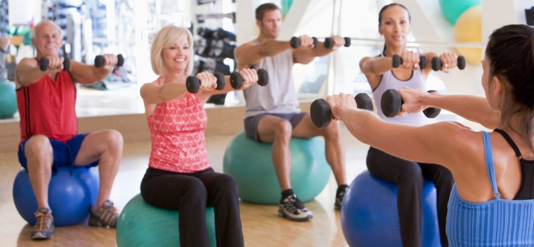 Mixed group in exercise class on gym balls with weights